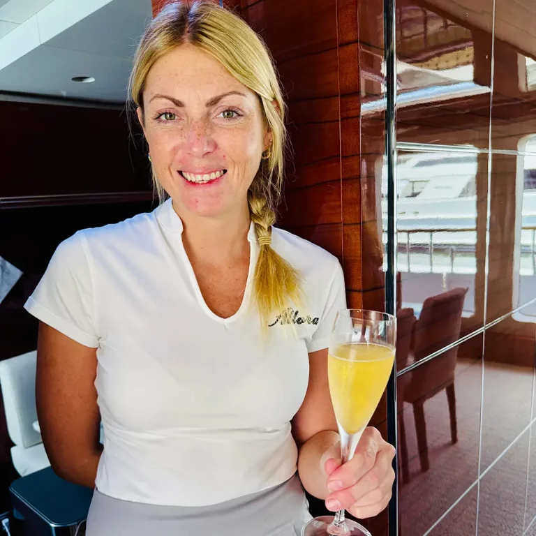 Crew member on Allora serving champagne with a smile